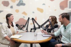 Three people around a table with microphones, podcasting