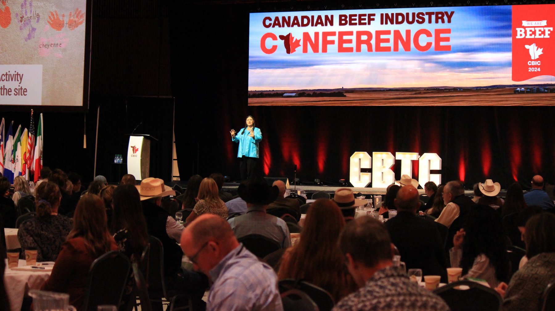 Becky McCray on a large stage with an audience including several wearing cowboy hats.