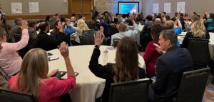 Becky McCray is speaking to a very full meeting room. Almost all the audience members are raising their hands.