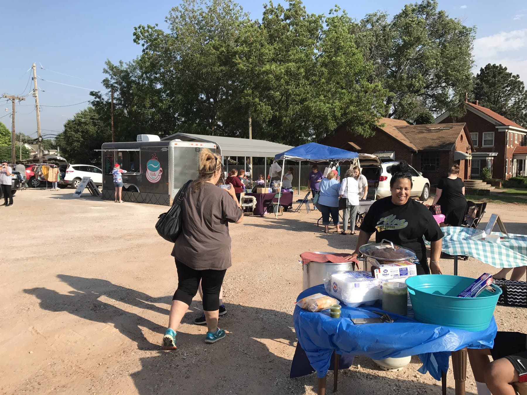 An empty lot with pop-up booths and a food truck, with diverse people enjoying the market.