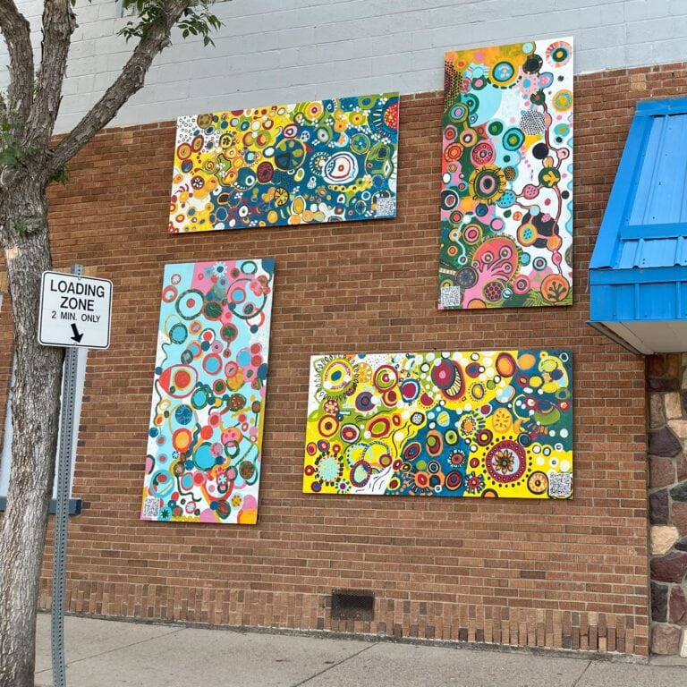 a brick wall downtown displays four colorful murals on boards.