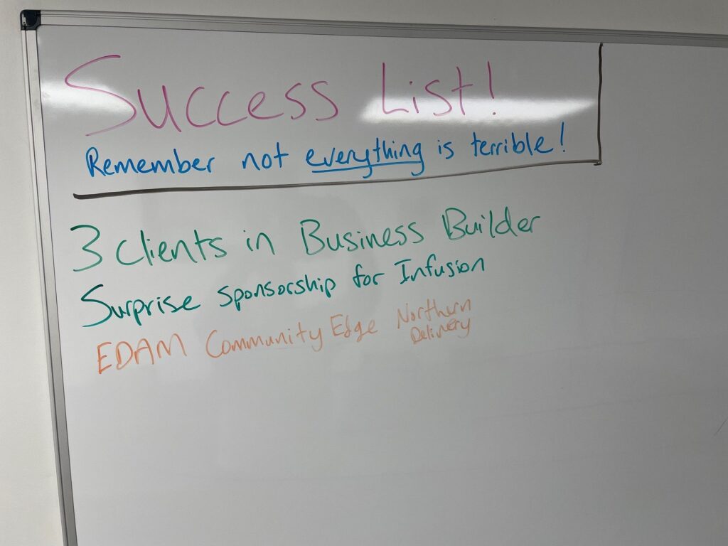 White board says, "Success List! Remember, not everything is terrible. Three clients in business builder. Surprise sponsorship for Infusion, EDAM Community Edge Northern Delivery."