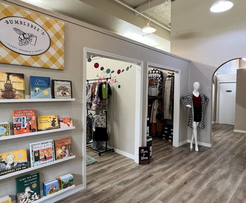 A retail building with walled spaces for individual businesses and a book rack on a wall. A well-dressed mannequin stands in the common area. 